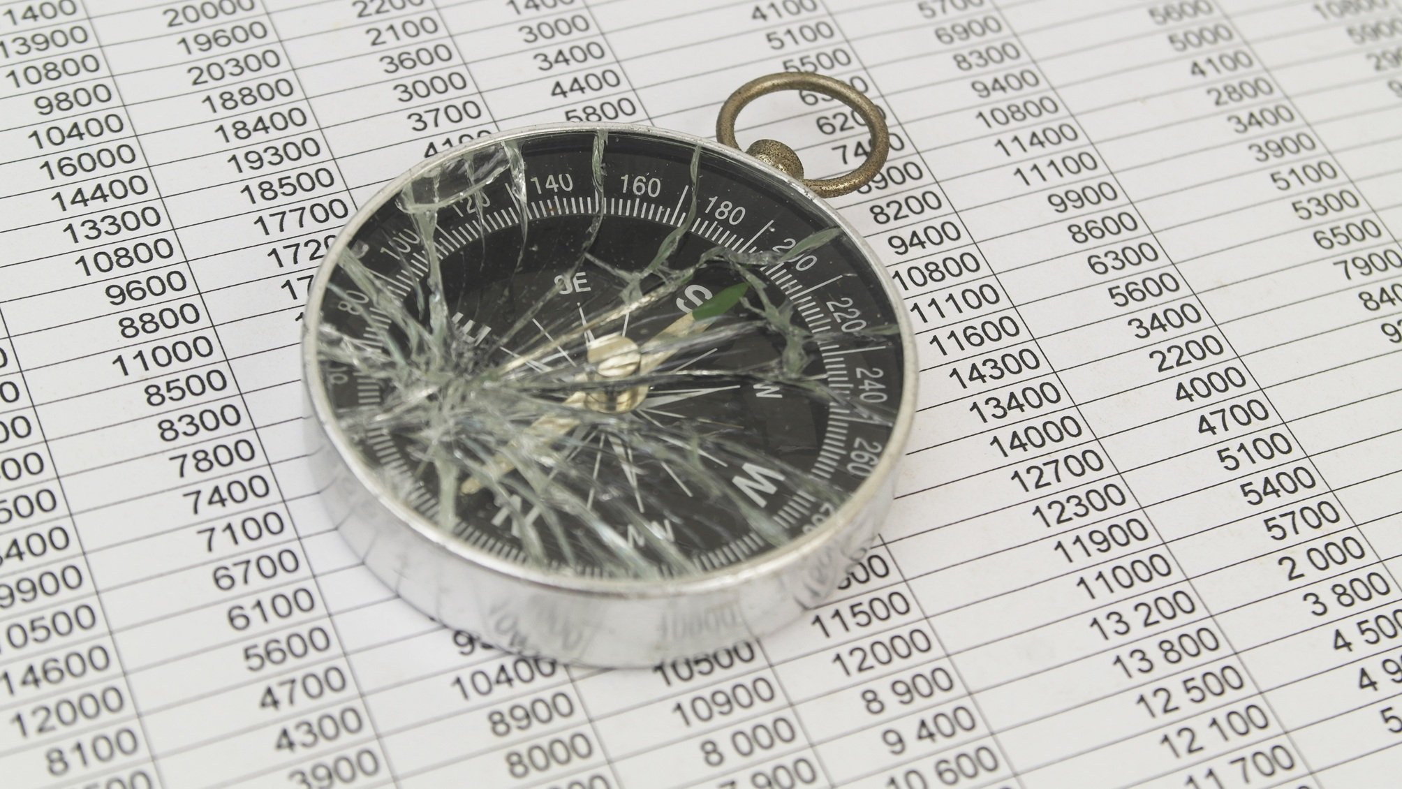 A smashed compass on top of financial paperwork.