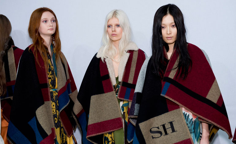 Three women wearing red, black and brown ponchos, one with 'SH' printed onto it