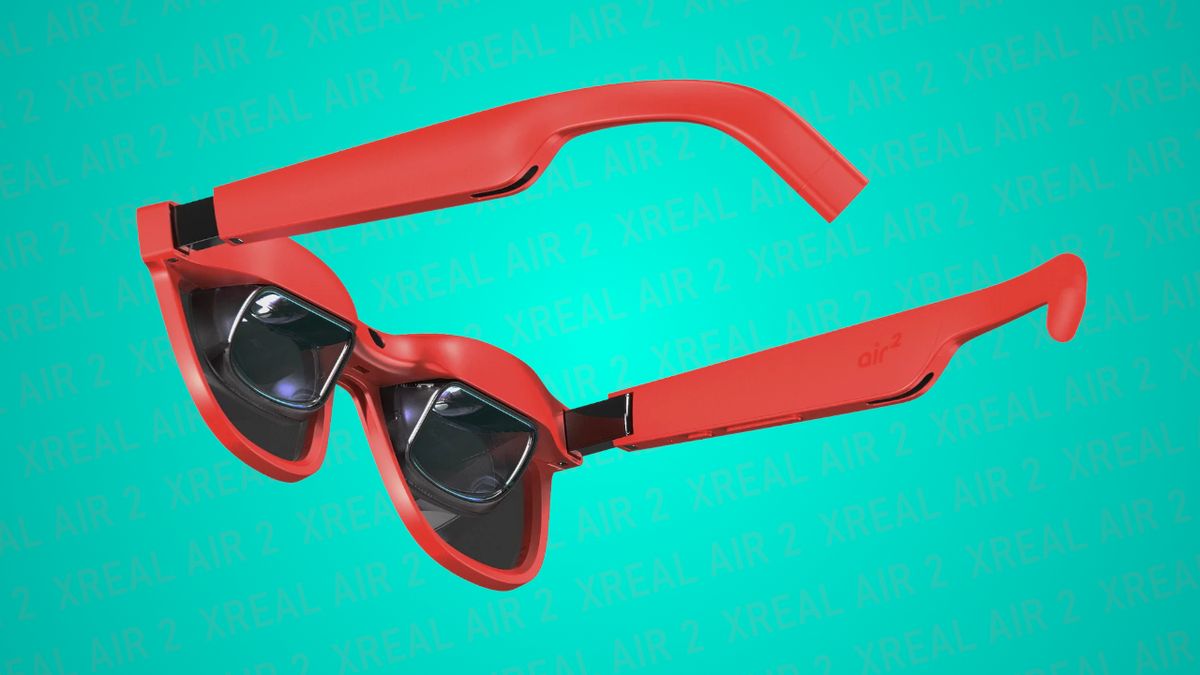 Image of XREAL Air 2 AR glasses, wearable displays that use bird bath optics to superimpose content into your field of vision, in red showing a 3/4 rear view of the optics and frames on a teal backdrop with the words &#039;XREAL Air 2&#039; repeated in the background.