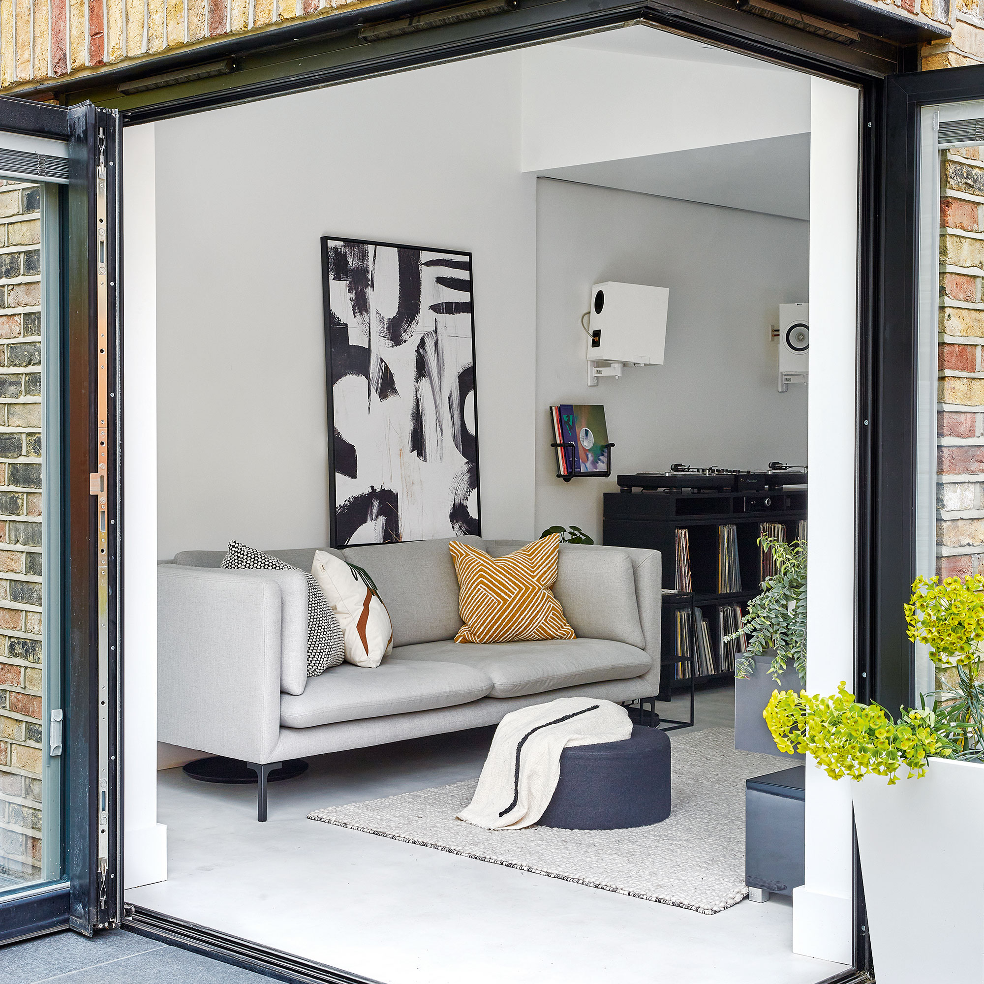 living room with white wall grey sofa with designed cushions painting frame on wall and book shelve