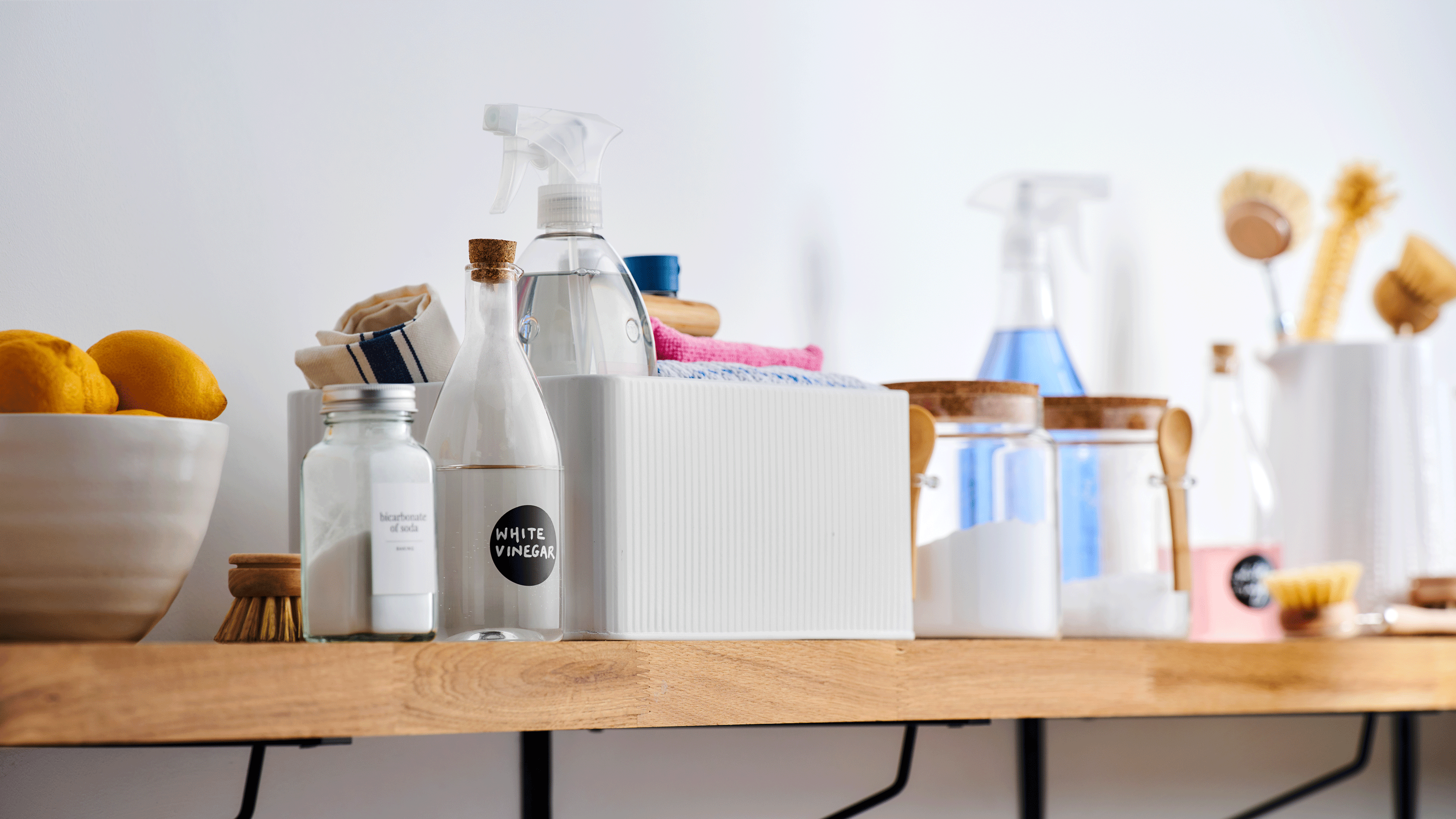 Shelf lined with cleaning products, some stored in a white enamel cleaning caddy