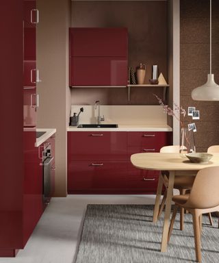 Red and blush kitchen with glossy red units, dining table to the side, off white countertops, pale grey floor, rug