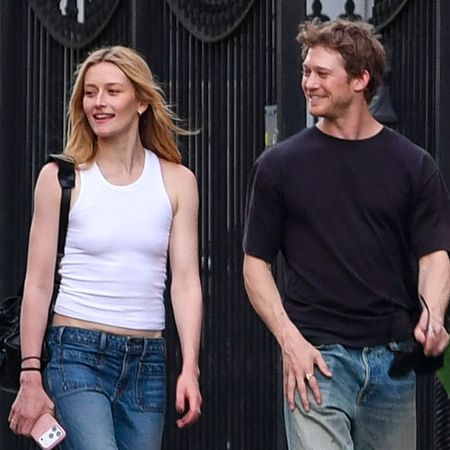 Sarah Pidgeon walks down the street in New York with Joe Alwyn wearing bootcut jeans with black ballet flats and a white tank top.