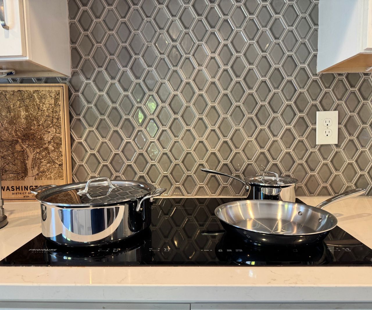 A set of three stainless steel drying pans on a black induction stove, viewed from the side.