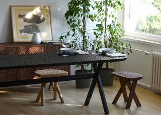 textured dining table in white room with pot plants and stools