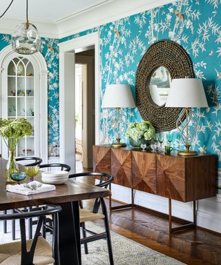 A dining room with large dark wooden sideboard, and turquoise and white wallpaper