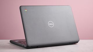 Back three-quarter view of Dell Chromebook 3120 open on desk with pink wall in background