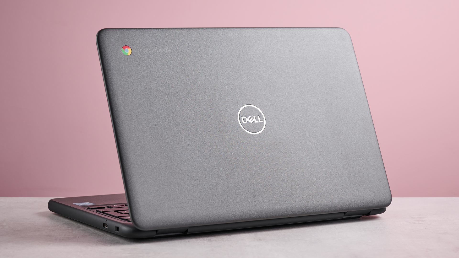 Back three-quarter view of Dell Chromebook 3120 open on desk with pink wall in background