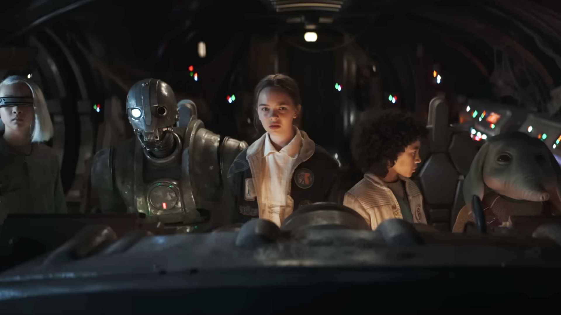 Young crew members and droids stand inside a dimly lit spacecraft in Star Wars: Skeleton Crew.