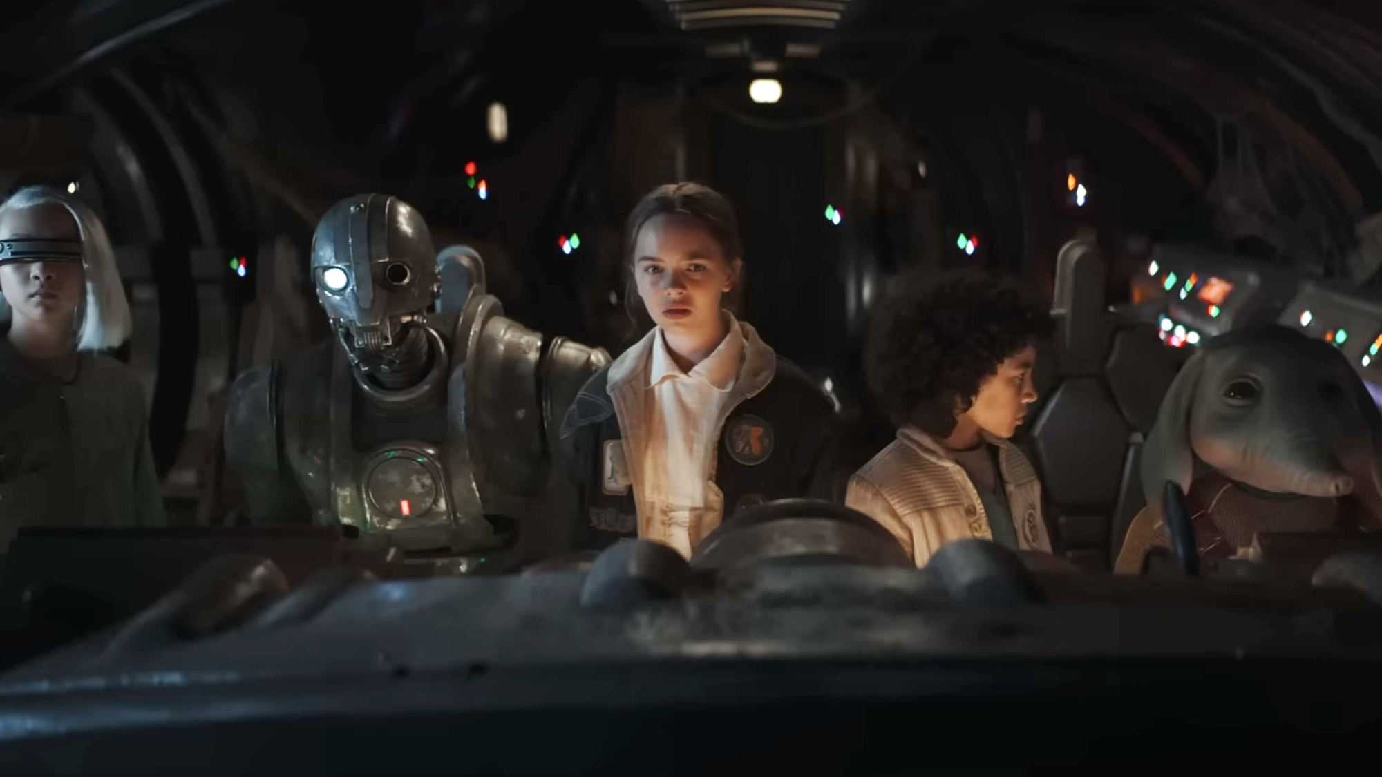 Young crew members and droids stand inside a dimly lit spacecraft in Star Wars: Skeleton Crew.