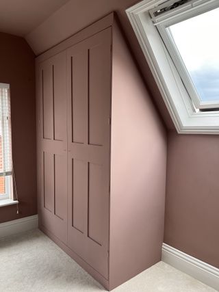 A purple attic room with a pitched ceiling and a painted built-in ikea pax wardrobe in the corner