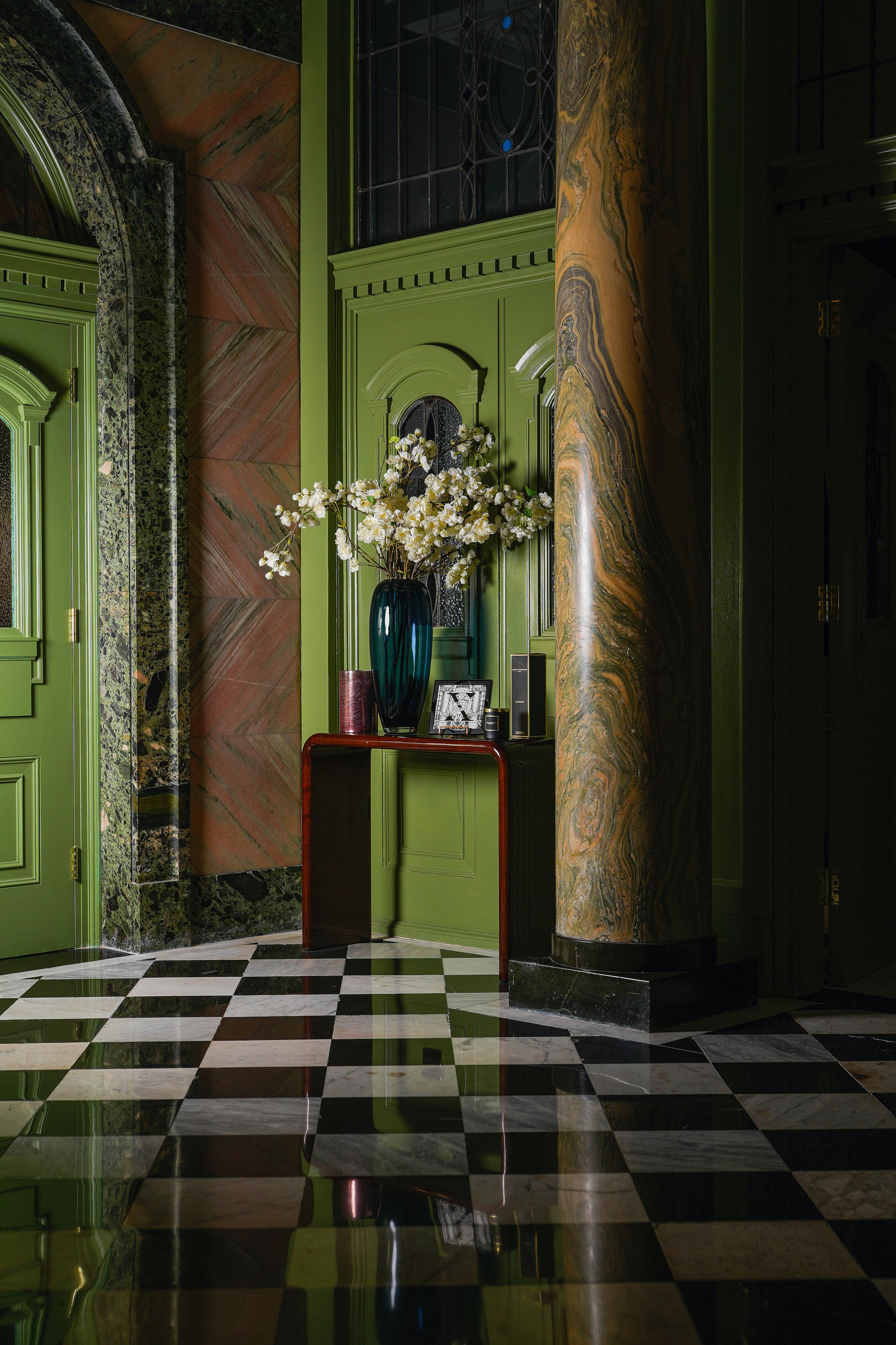 Hotel lobby with black and white checkerboard floor, green and orange marble architectural details and a burgundy gloss console table