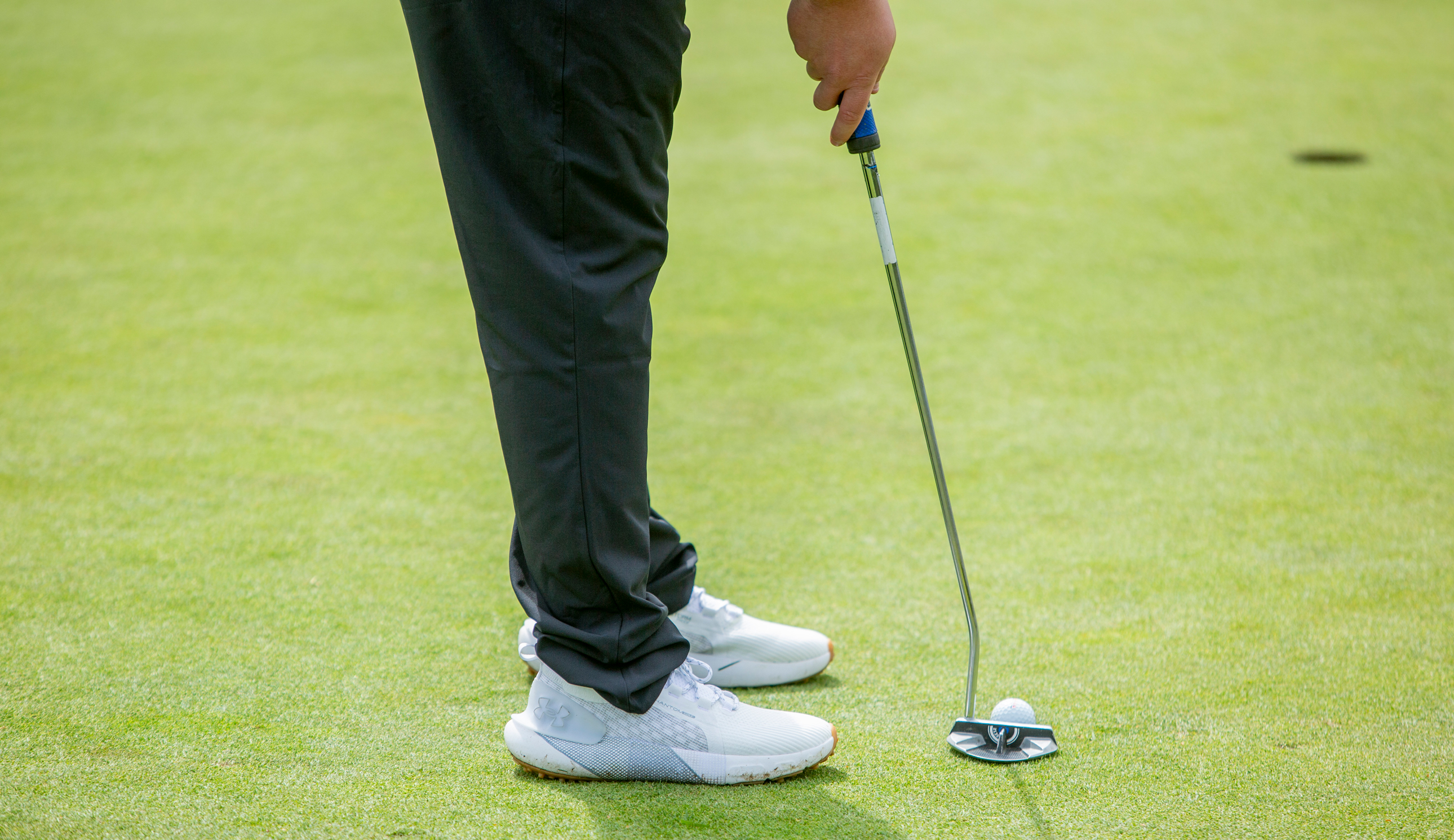 A close-up of a putter and golf shoes