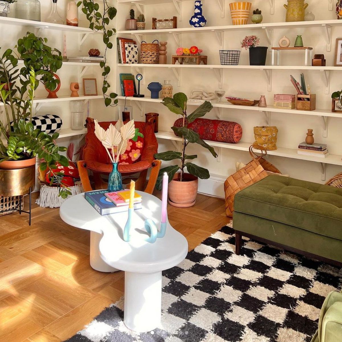 Meja kopi putih melengkung dengan buku dan lilin di ruang tamu yang terang