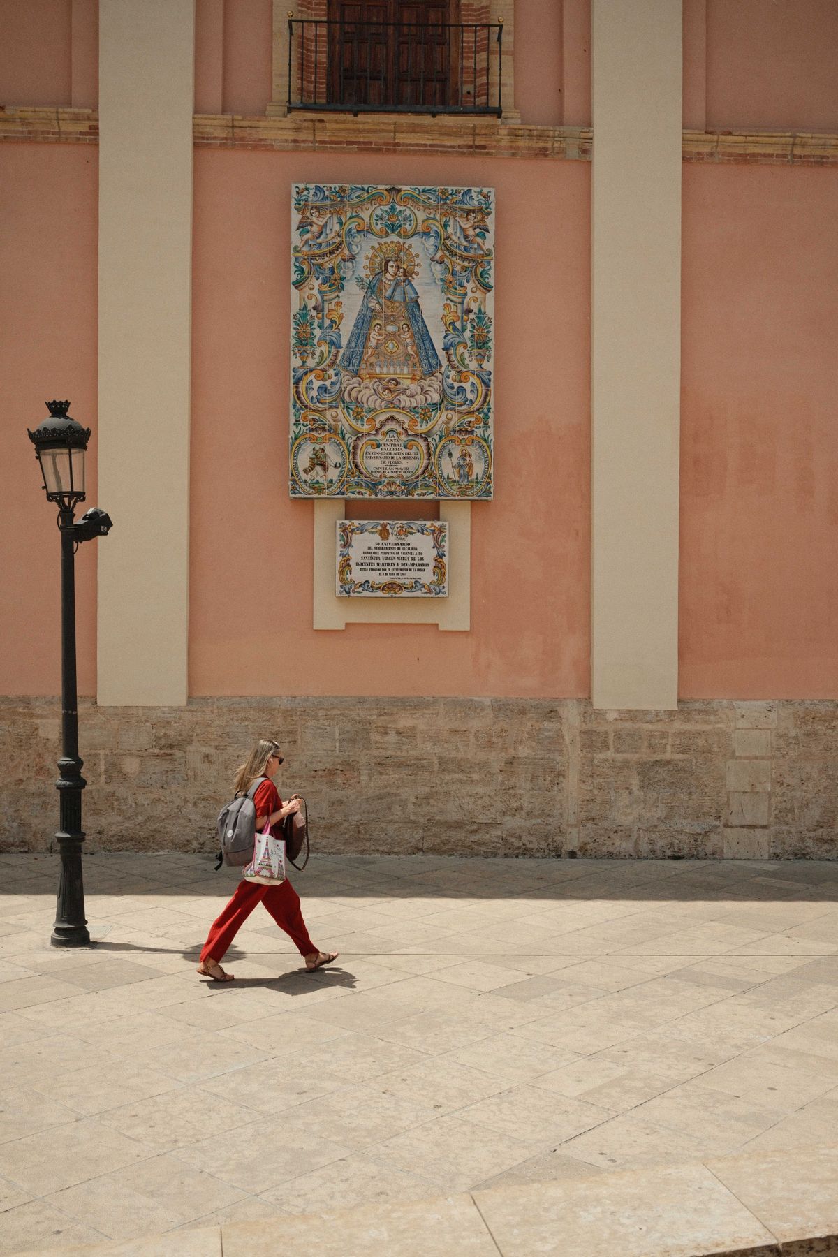 A woman walks in front of a pink pastel wall with a mosaic