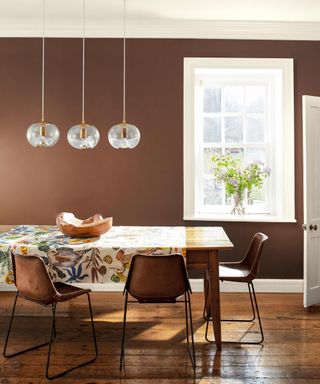 dining room with brown wall, white trim, wooden flooring and table with tablecloth and brown chairs