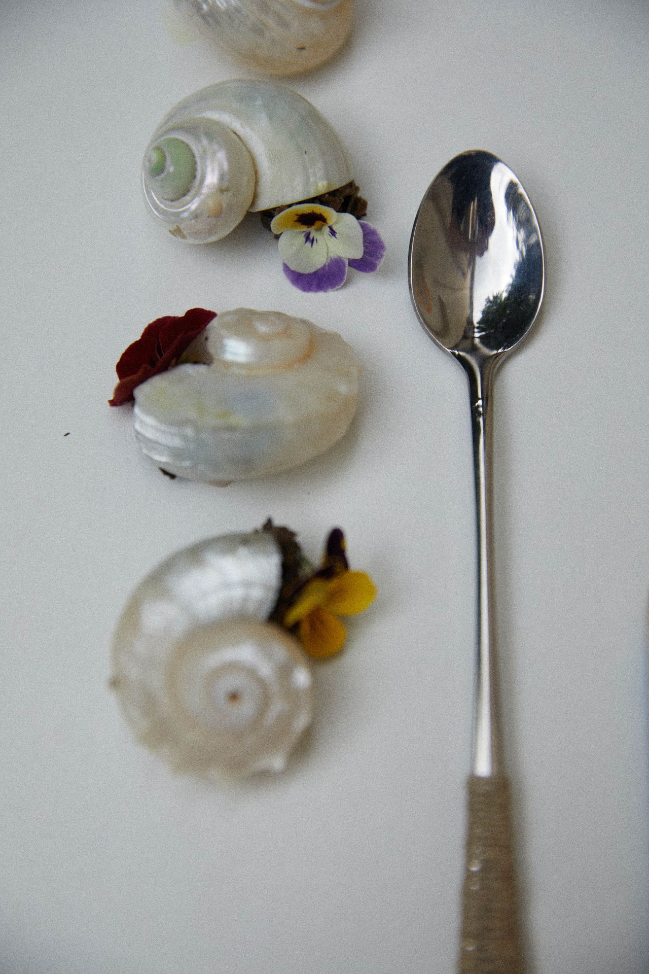 A series of couscous food sculptures, snails, shells, and tomatoes is beautifully positioned on a white cloth table along with silver and wooden cutlery.