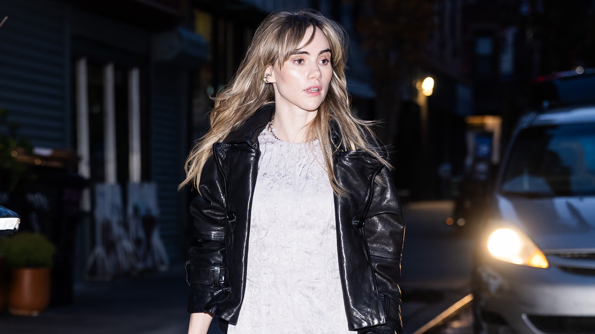 Suki Waterhouse wearing a black leather jacket, mini dress, and slouchy ankle boots
