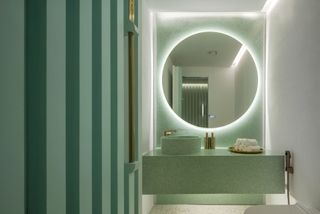 Restroom with green terrazzo surfaces, striped walls and round backlit mirror at Infinity Wellbeing, Bangkok