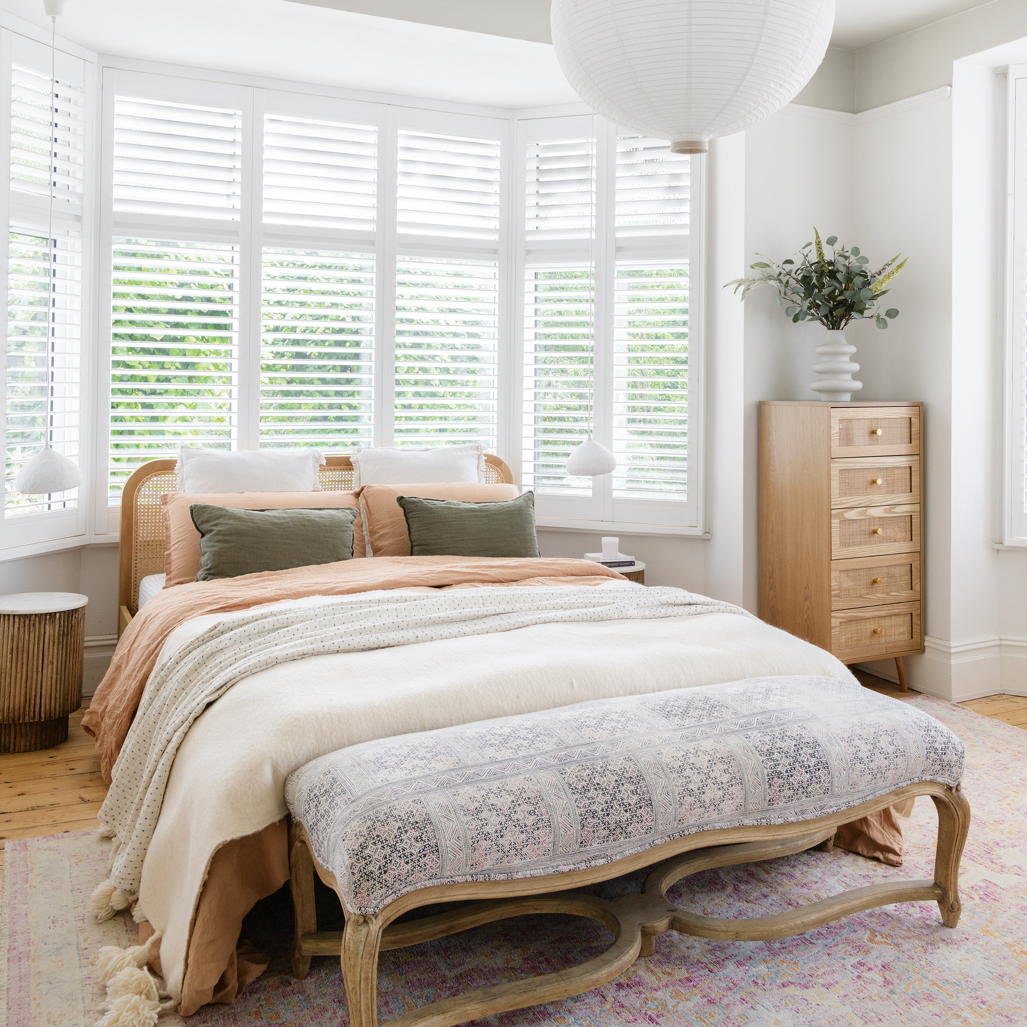 a neutral coloured bedroom with a wooden bed frame, wooden tall boy and bay windows with fitted shutters
