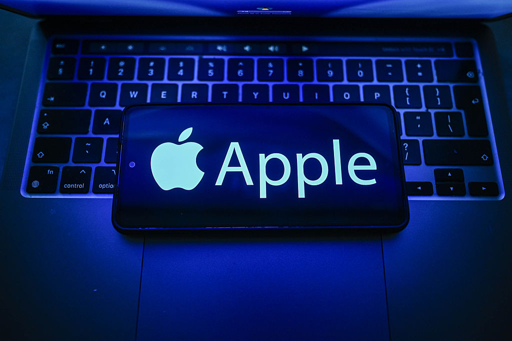 An Apple logo is seen displayed on a smartphone on the top of a laptop.