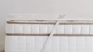 Image shows the Saatva High-Density Foam Mattress Topper placed on a Saatva innerspring mattress