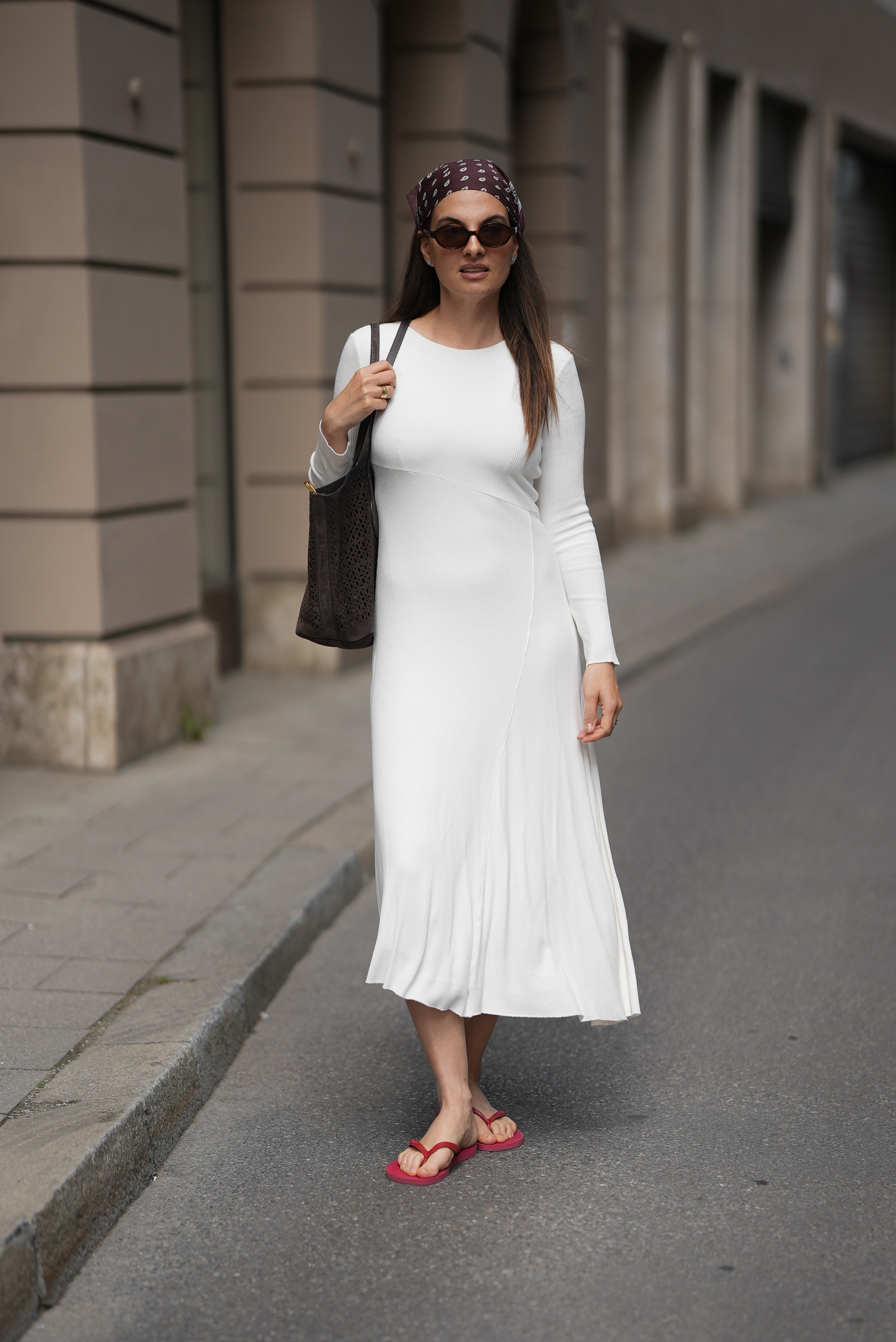 A woman wears a headscarf, a white dress, and red flip-flops.