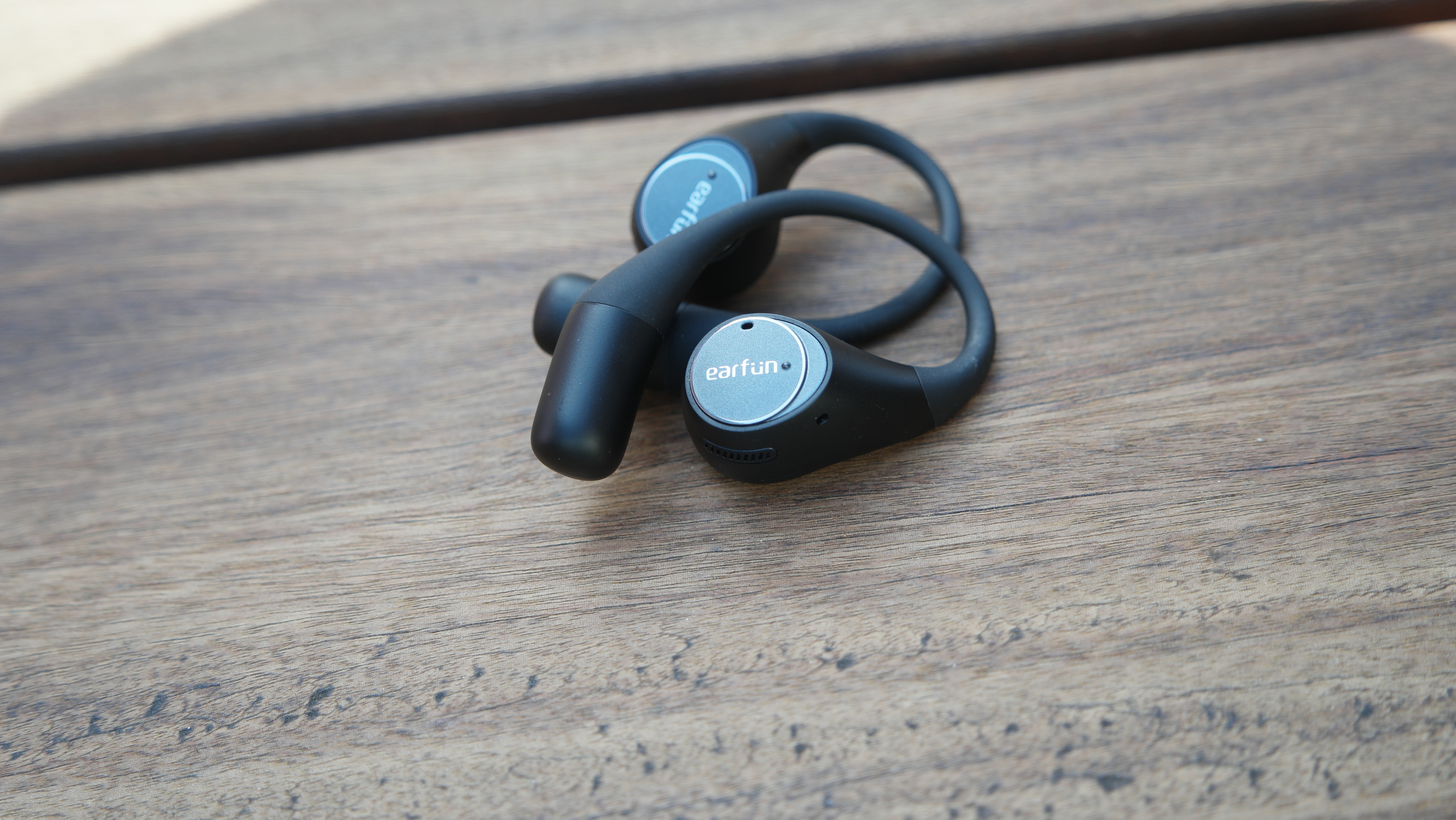 EarFun OpenJump earbuds on top of each other on a wooden deck