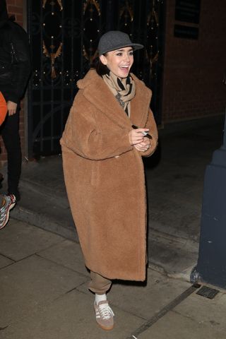 A photo of Lily Collins signing autographs in a Max Mara teddy coat and Adidas sneakers.