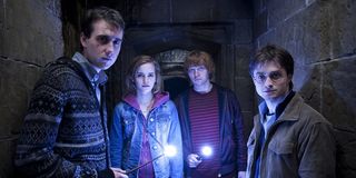 Neville Longbottom, Hermione Granger, Ron Weasley and Harry Potter hold their lit wants in the hallw