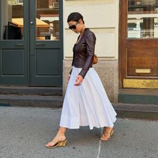 Aisha wears white dress, leather jacket, and wedged heels. 
