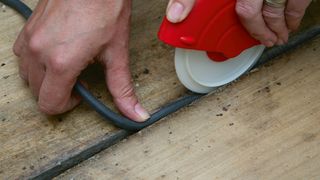 Person inserting draft strips between floorboards