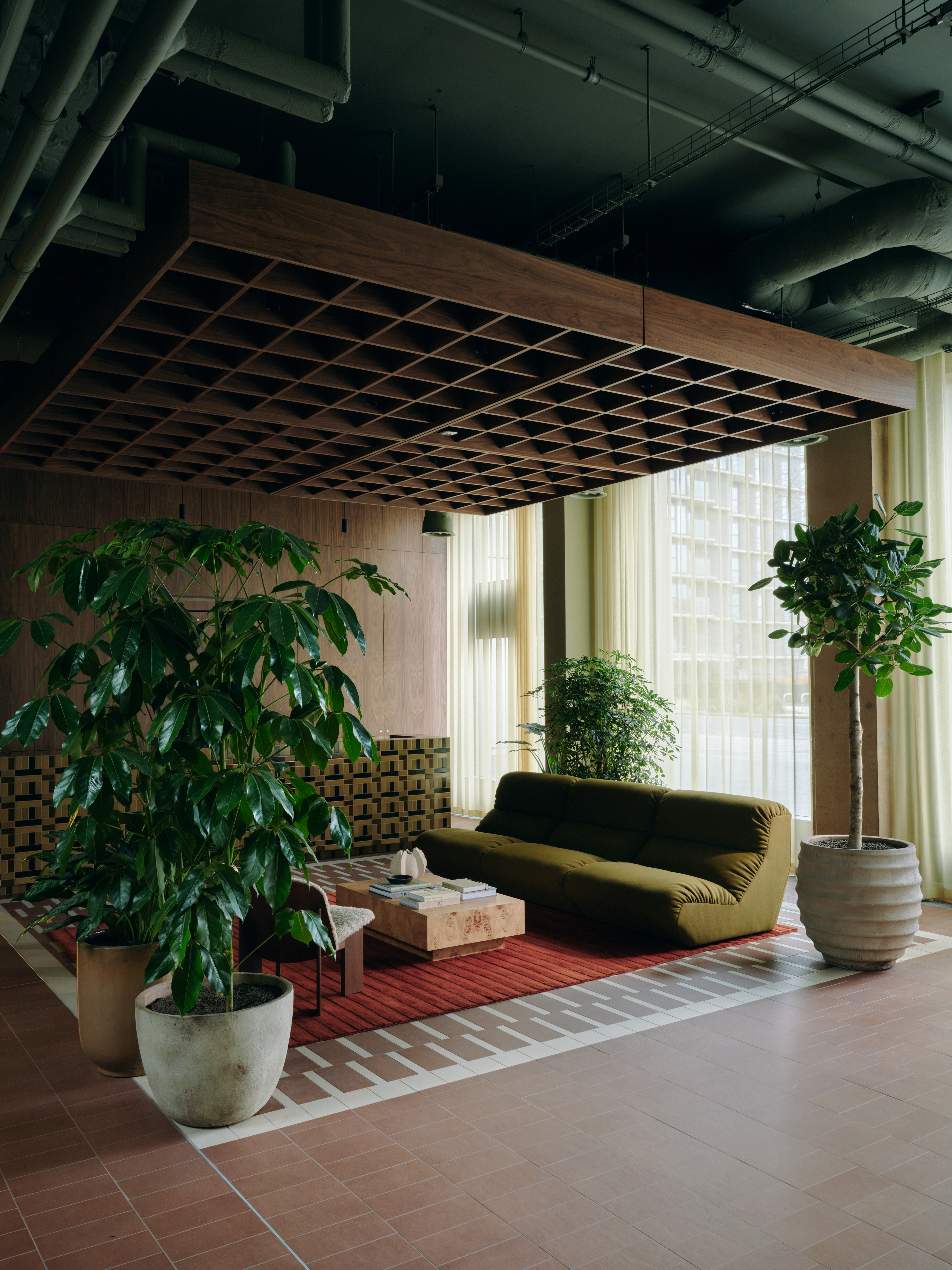A series of interior shots of a workspace designed with terracotta-hued checkered floors, coffered ceilings in wood and back-lit blocks, pendant, see-through lighting, mid-century furniture,