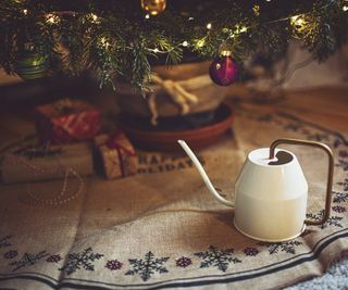 A white watering can next to a Christmas tree