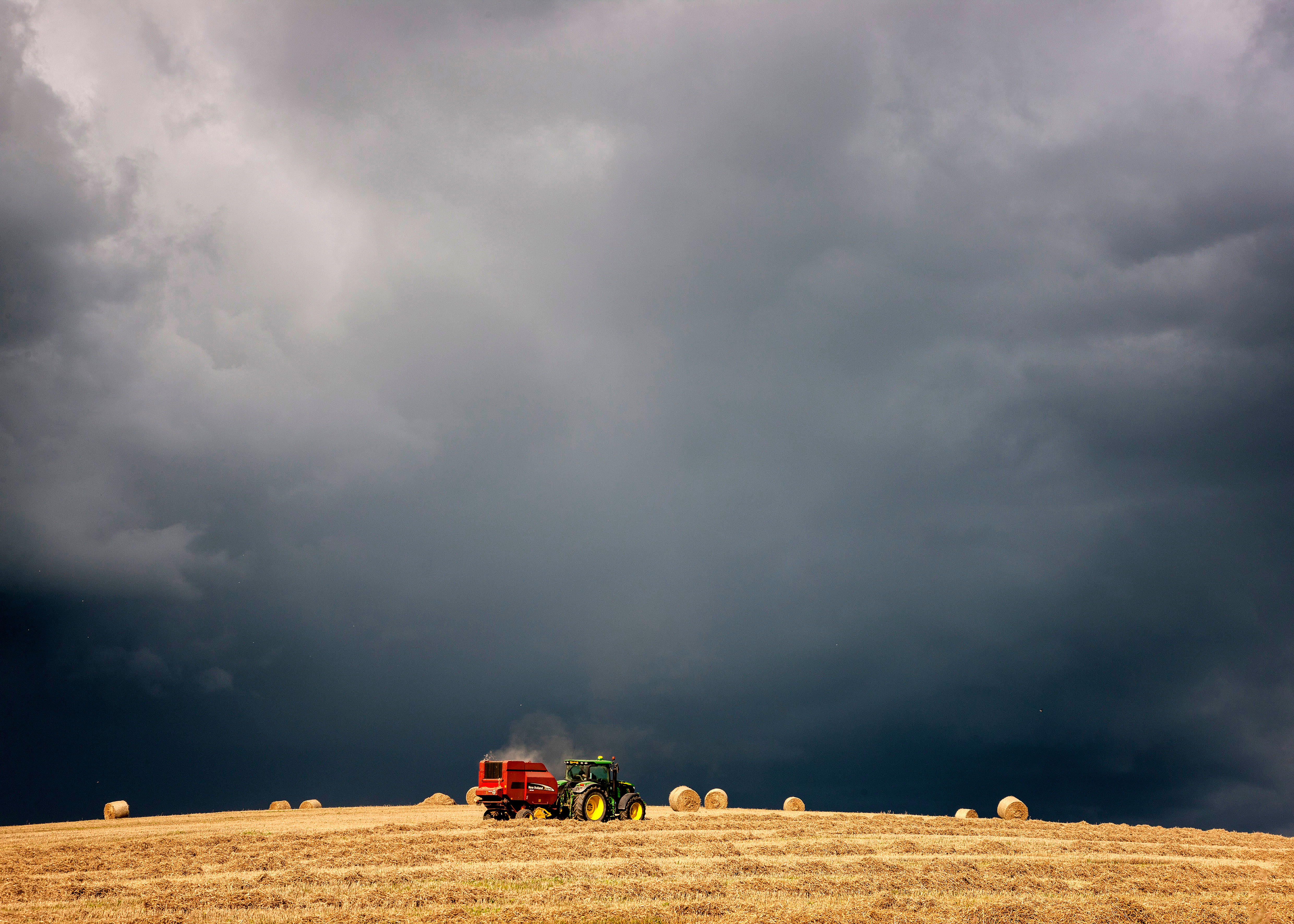 A tractor collecting hay bales under dark black stormy sky.