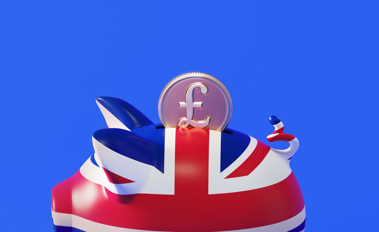 Piggy bank textured with British flag and pound coin over blue background. Horizontal composition with copy space.