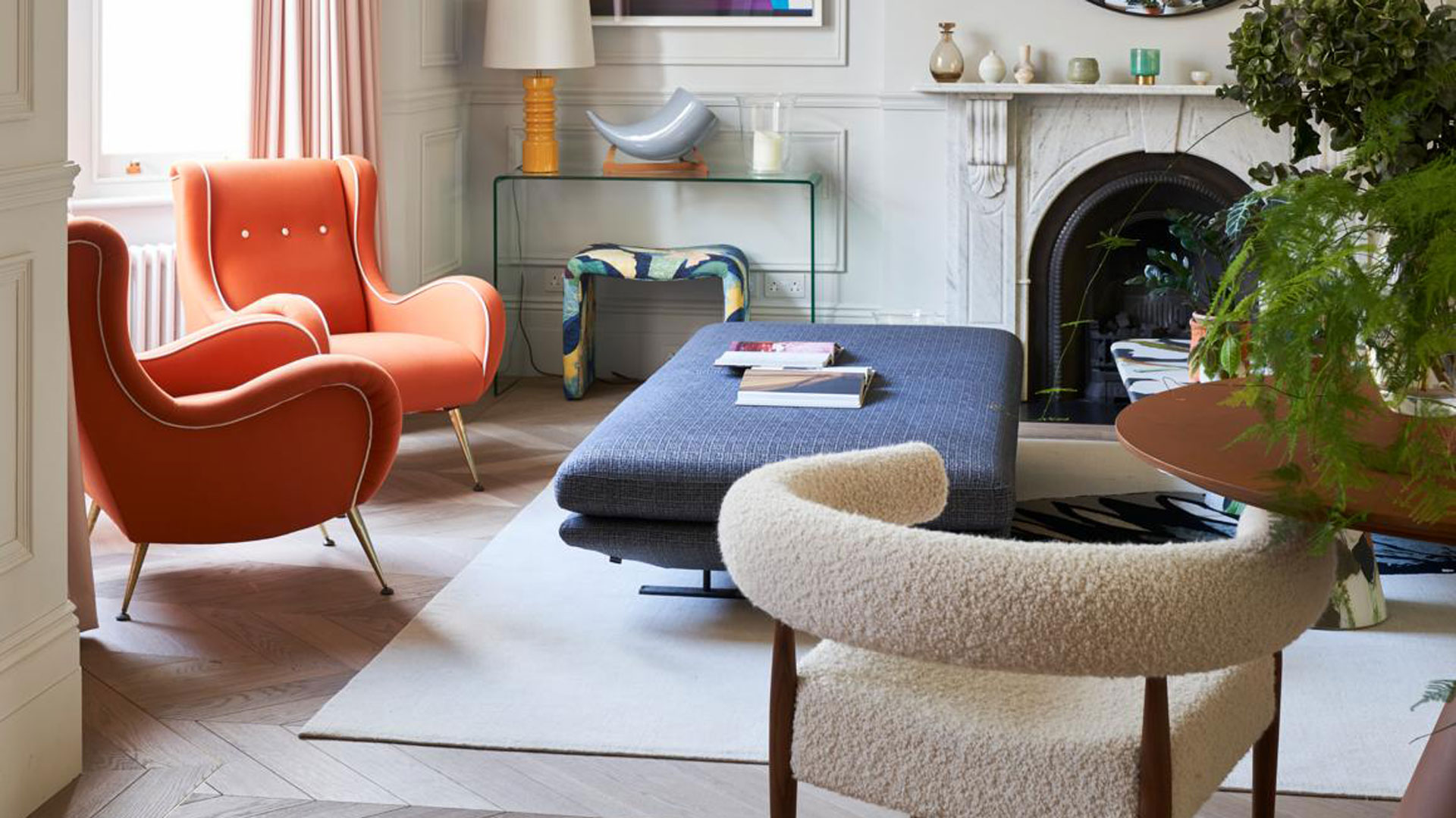 contemporary living room with orange armchairs, blue upholstered footstool and a boucle dining chair