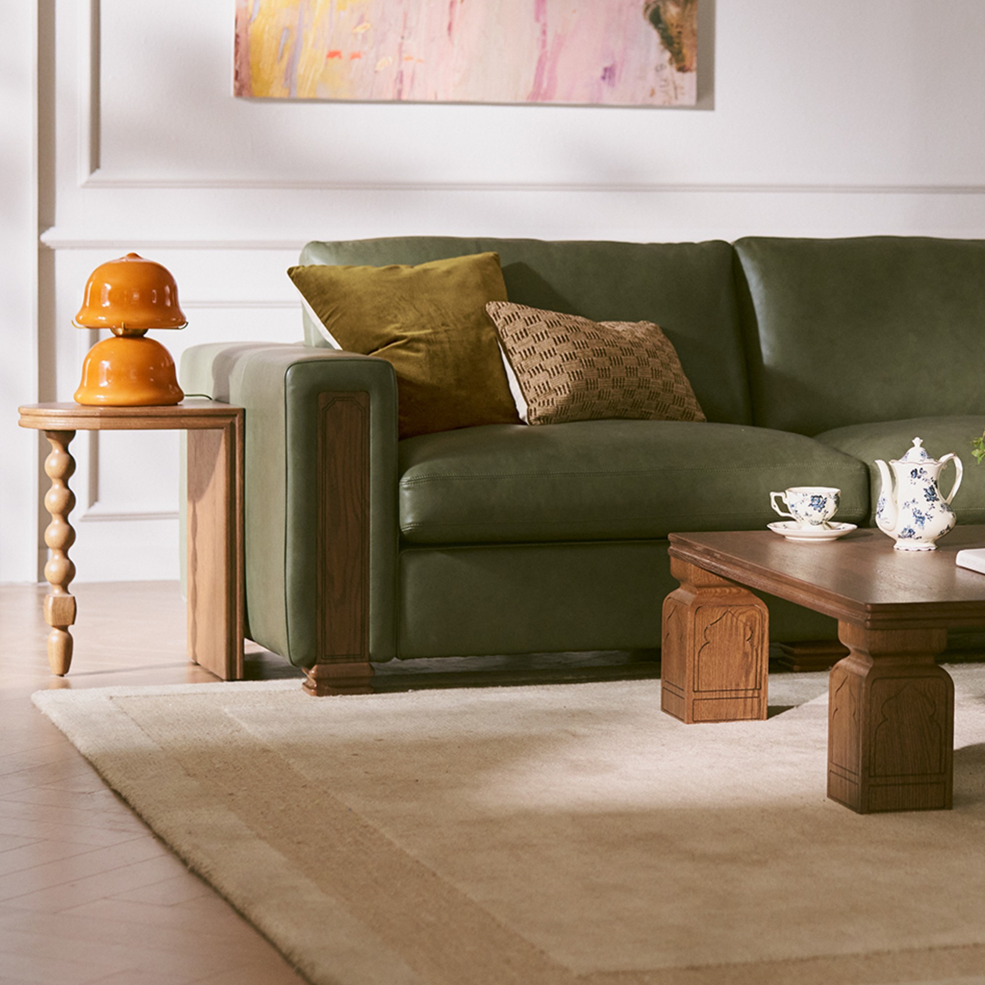 The Kagan sofa from Tan France's Castlery collection in green leather with a wooden coffee table and side table with an orange table lamp on top