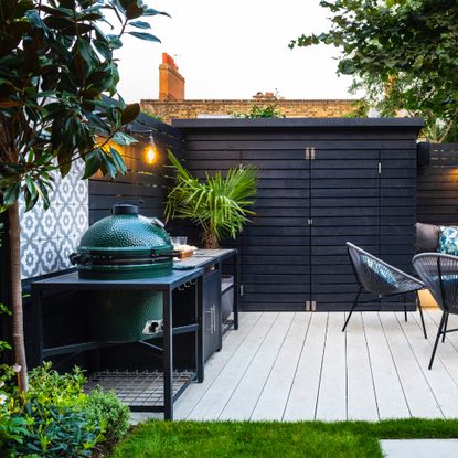 outdoor kitchen with Big Green Egg BBQ, shed, storage units, decking, plant, table and chairs, tiled wall area 