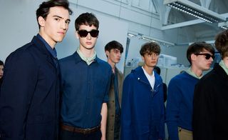 Male models wearing Margaret Howell S/S 2015 collection. All dressed in navy / blue. The model on the left is dressed in a navy suit. The model next to him is wearing sunglasses. The two models next to them are wearing a blue overcoat and a blue jersey respectively.