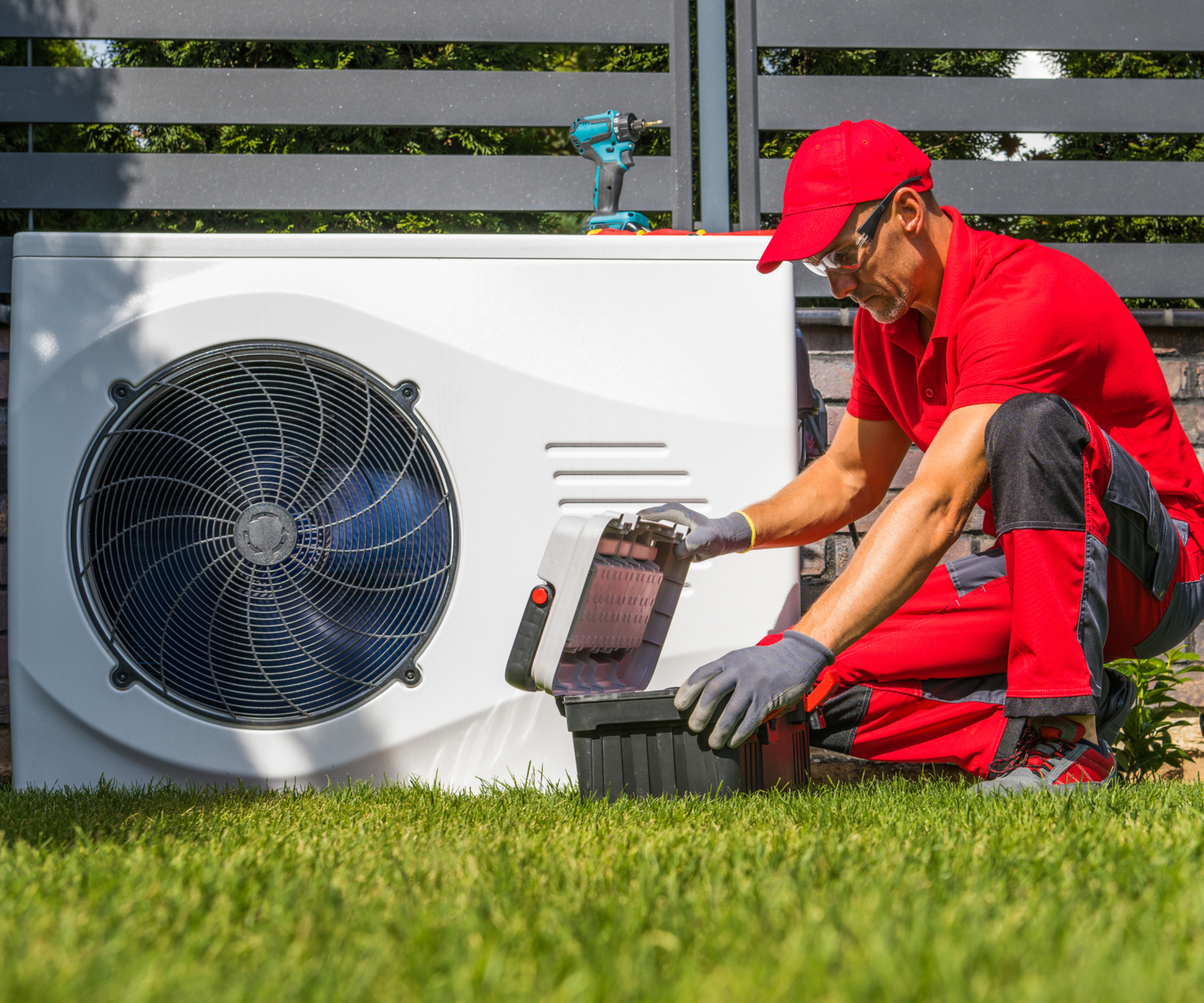 heat pump installer kneeling in front of heat pump in garden