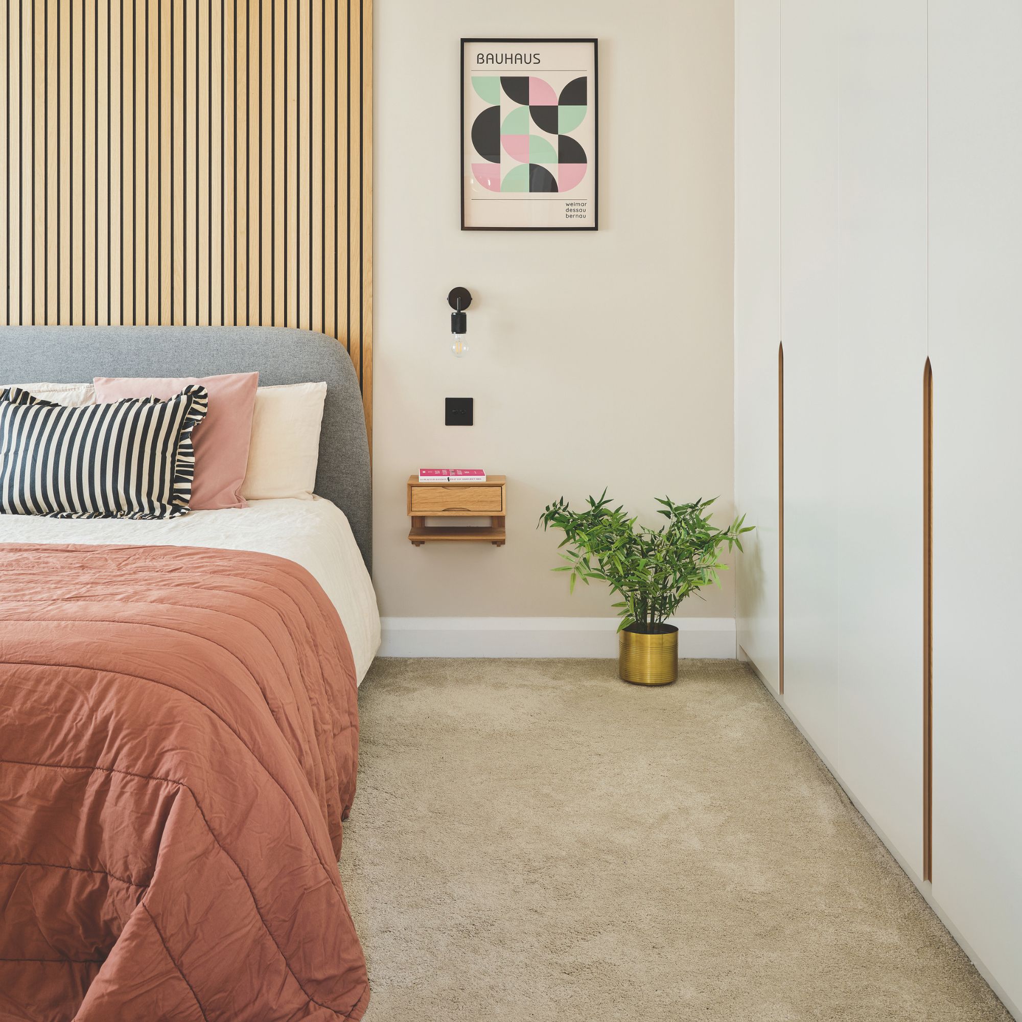 Cream painted bedroom with a beige carpet and white fitted wardrobes on the right. There's a bed with wall panelling behind it on the left
