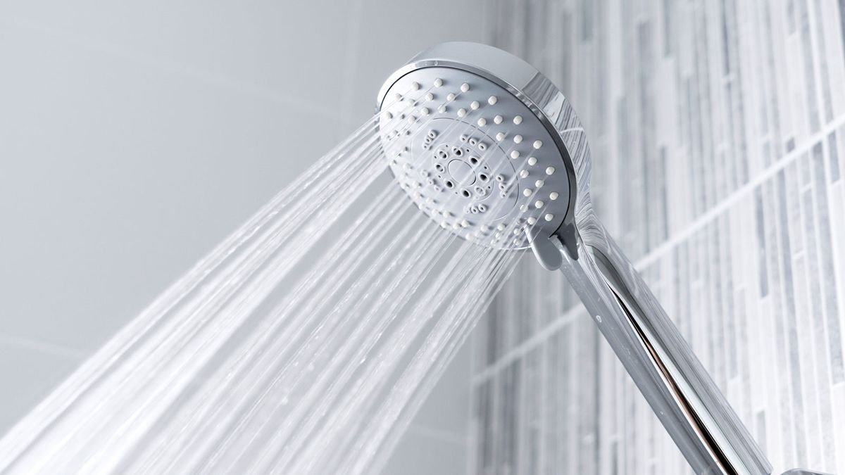 Chrome shower head with water slowing out on shades of grey tile background