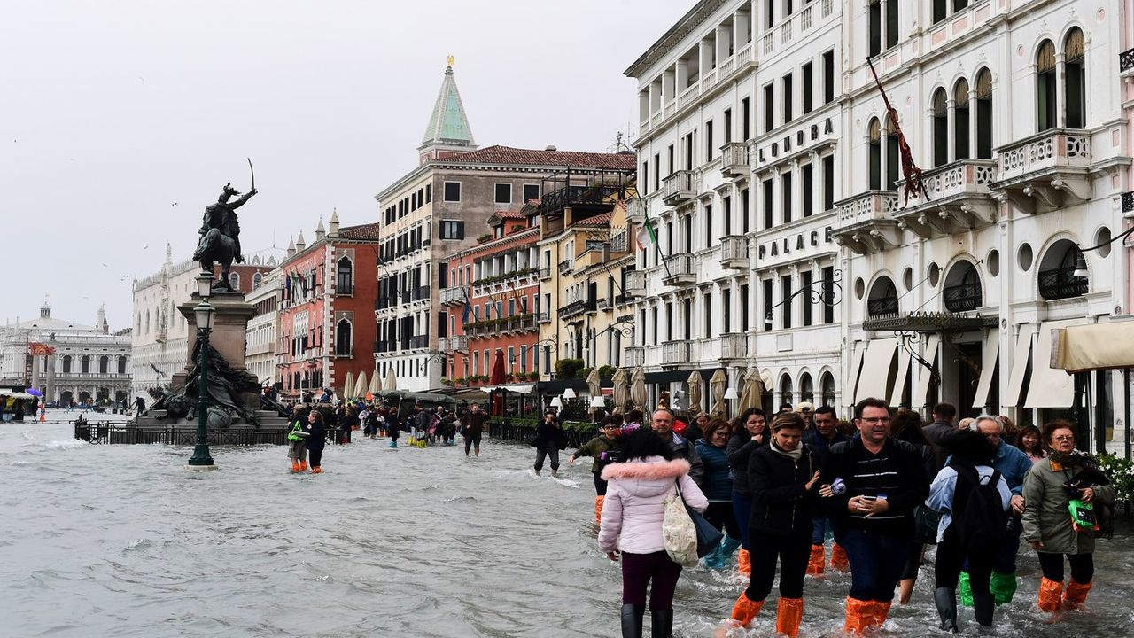 People walk in the flooded Riva degli Schiavoni during a high-water (Acqua Alta) alert in Venice on October 29, 2018. - The flooding, caused by a convergence of high tides and a strong Sirocc