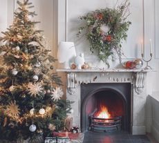 A white living room with a fireplace with a wreath above it and a Christmas tree