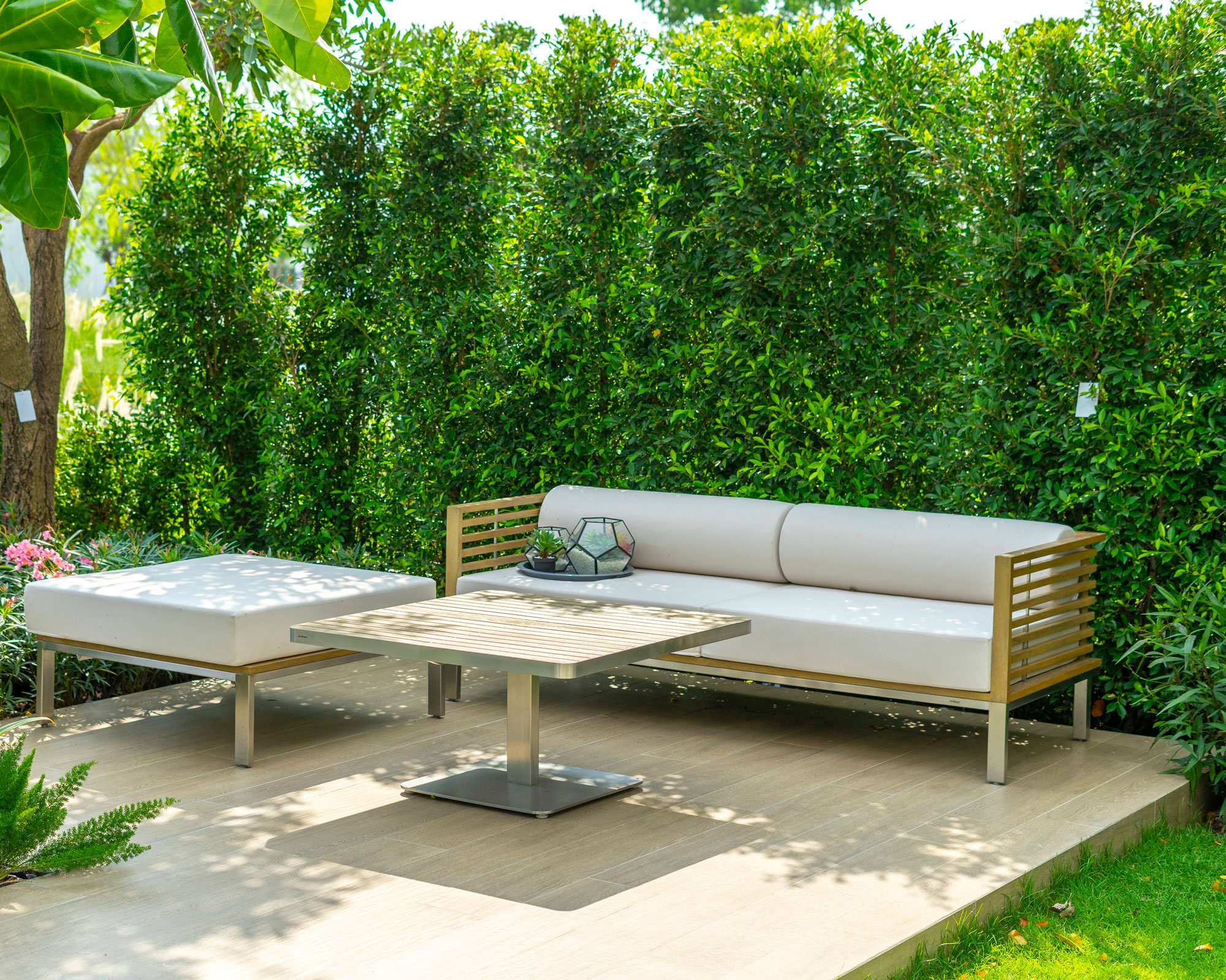 tall screening hedge with garden sofa, stool and talbe on deck edged with lawn