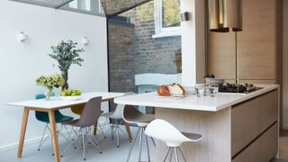 a modern kitchen extension with a sleek marble and wood island, wooden cabinets, a glass roof in the extension and a white dining table with flowers on top