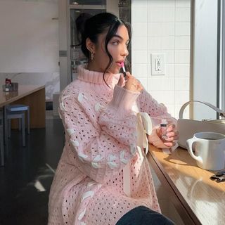 Mobina Peiman applies Dior Lip Glow Oil while wearing a pink sweater with bow details