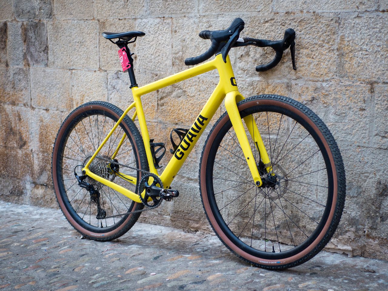 A yellow Guava Spot gravel bike leans against a wall