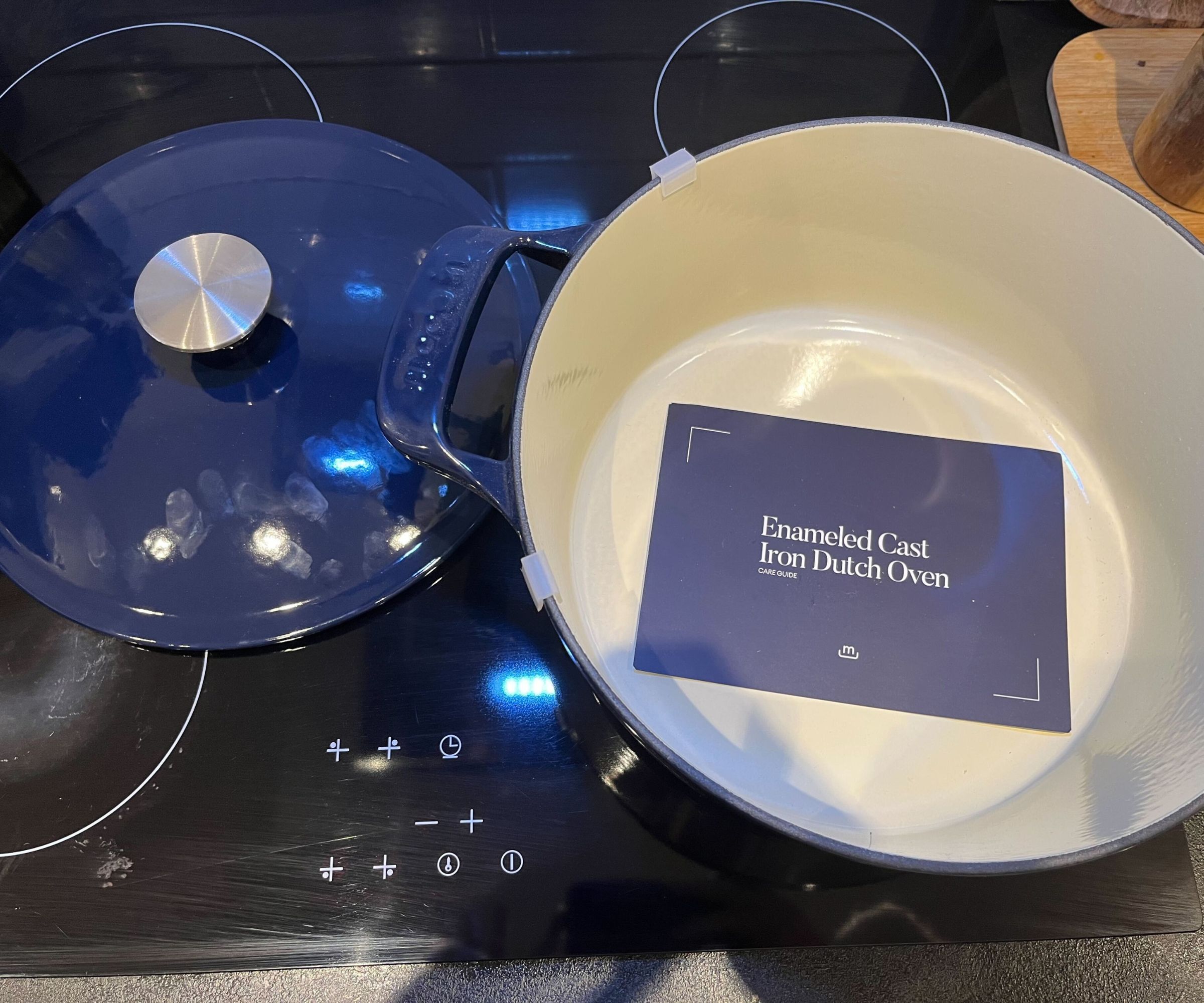 The blue Made In Dutch Oven on a black electric stove top wit the lid beside it. A blue piece of paper in the base with the name of the product written on it